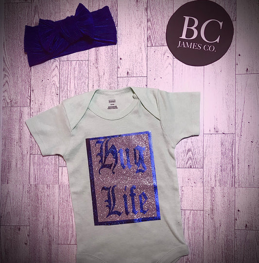 Teal “HUG LIFE” onesie with royal blue binki clip and bow headband