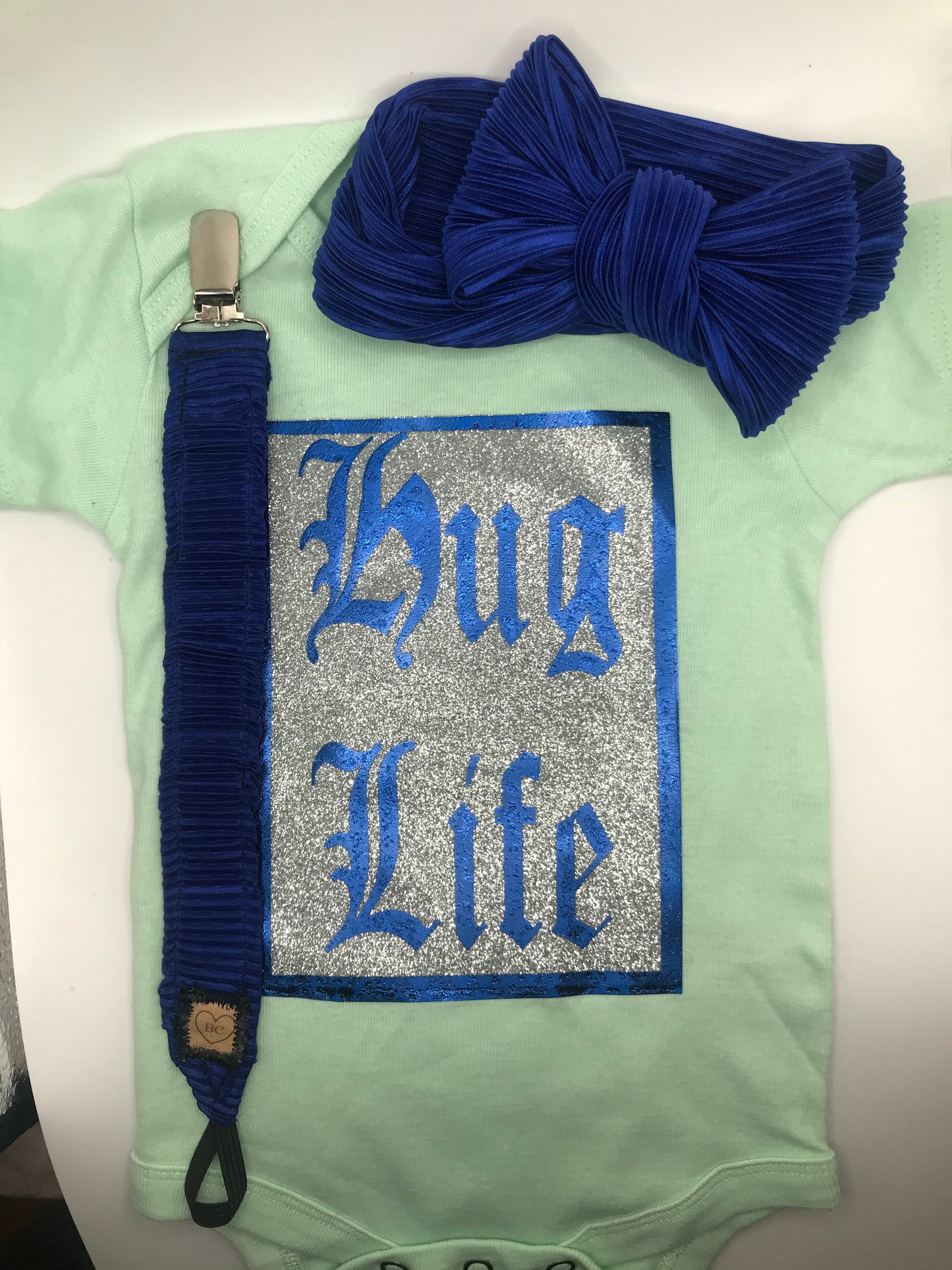 Teal “HUG LIFE” onesie with royal blue binki clip and bow headband