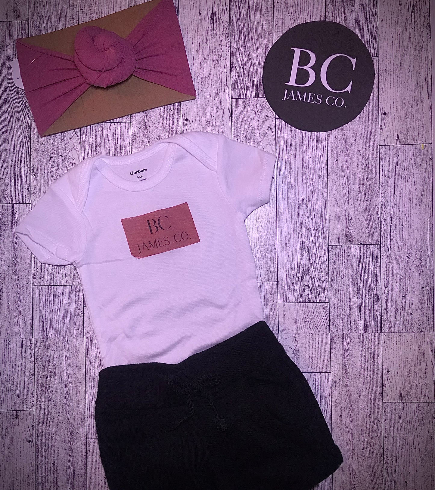 B.C JAMES CO. onesie with pink turban donut style headband and black shorts